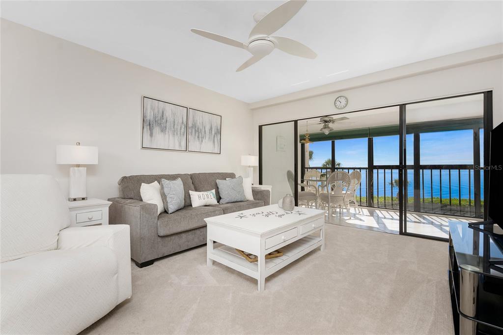 A living room features a gray sofa, white coffee table, and sliding doors overlooking the ocean — 1551 BEACH ROAD UNIT 306, ENGLEWOOD, FL