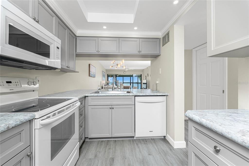 A kitchen with gray cabinets, white appliances, and light-colored countertops overlooking a living area — 1551 BEACH ROAD UNIT 306, ENGLEWOOD, FL