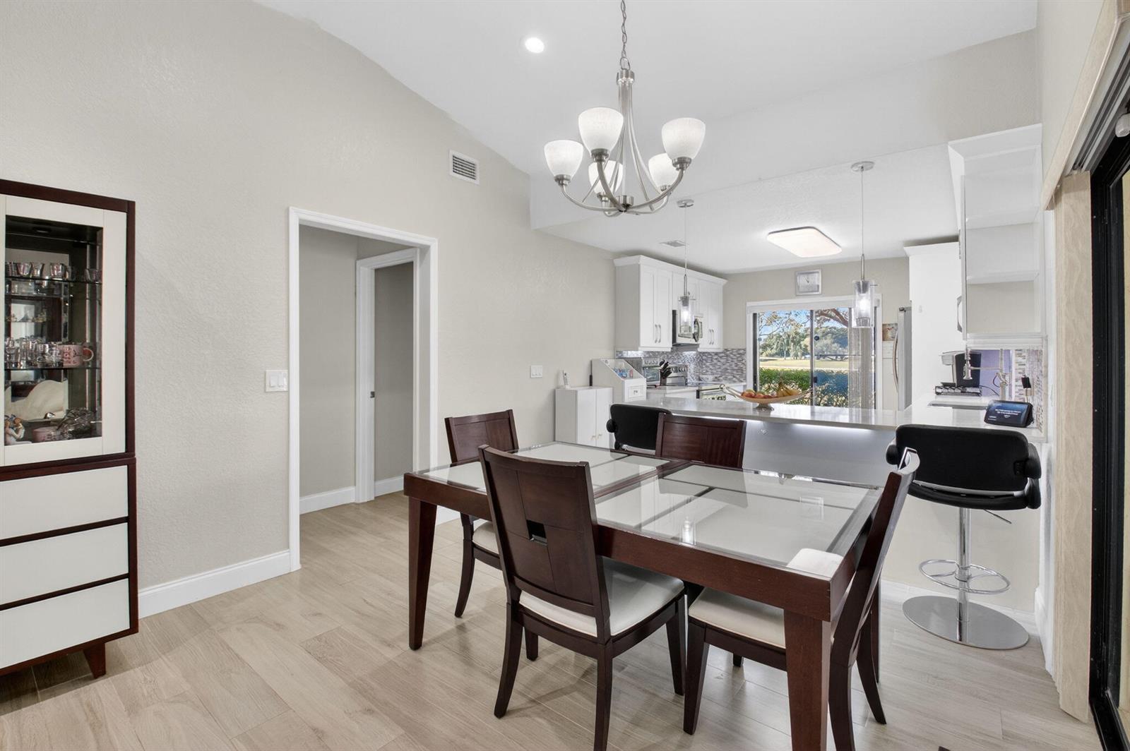 A dining area with a glass-topped table, dark wood chairs, and an adjacent kitchen island — 5750 Parkwalk Circle E, Boynton Beach FL 33472, BOYNTON BEACH, FL
