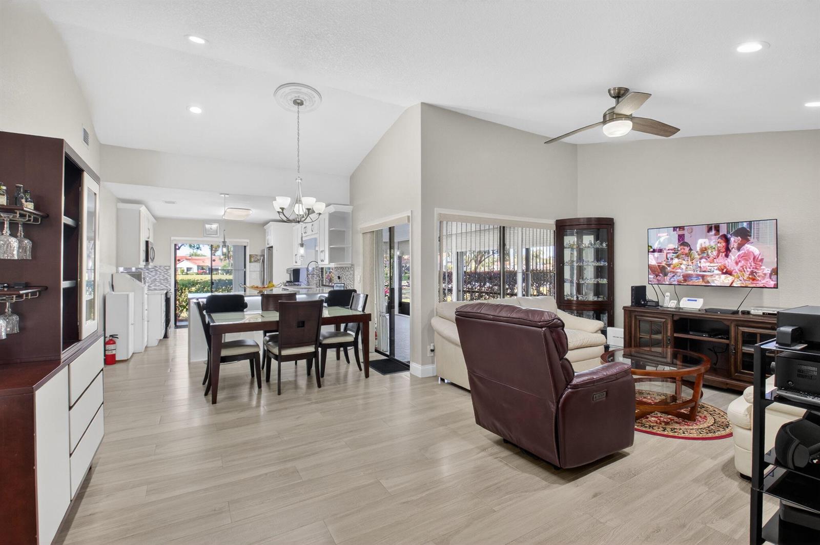 An open-concept living and dining area features light wood flooring, a vaulted ceiling, and furniture — 5750 Parkwalk Circle E, Boynton Beach FL 33472, BOYNTON BEACH, FL