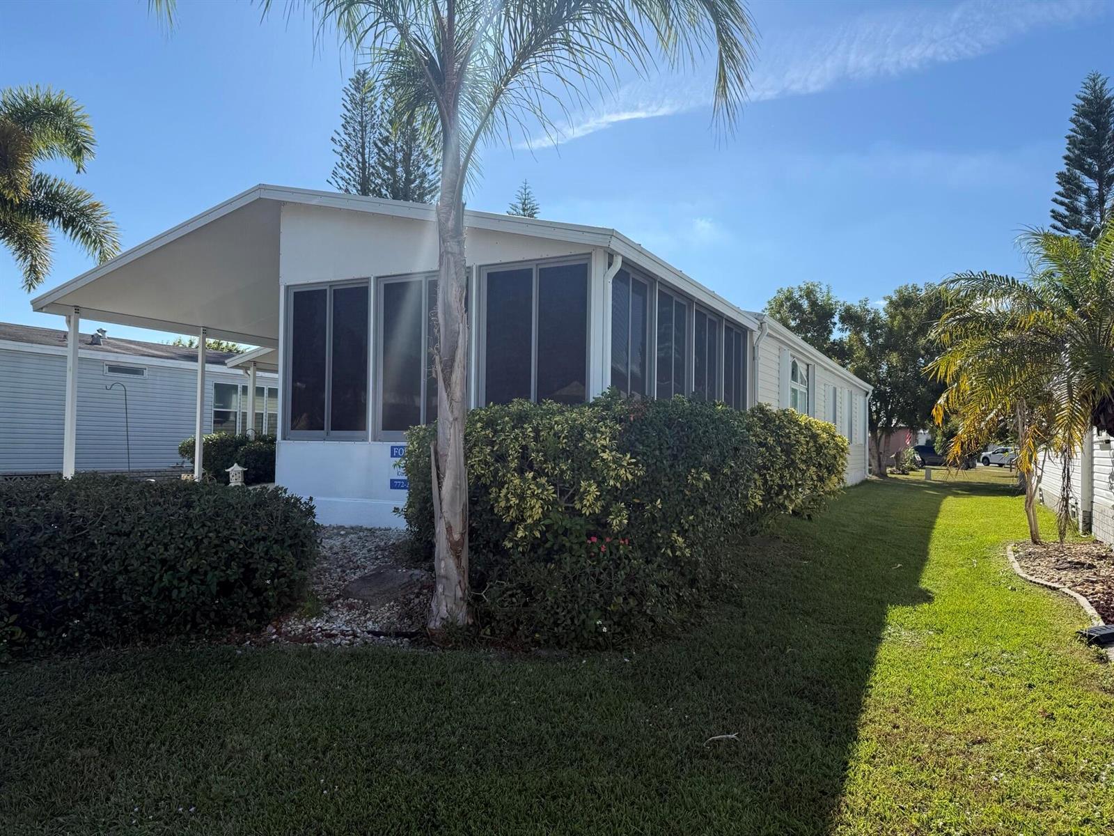 A white mobile home features a screened-in porch, a carport, and surrounding landscaping — 6615 Spanish Lakes Boulevard, Fort Pierce FL 34951, FORT PIERCE, FL