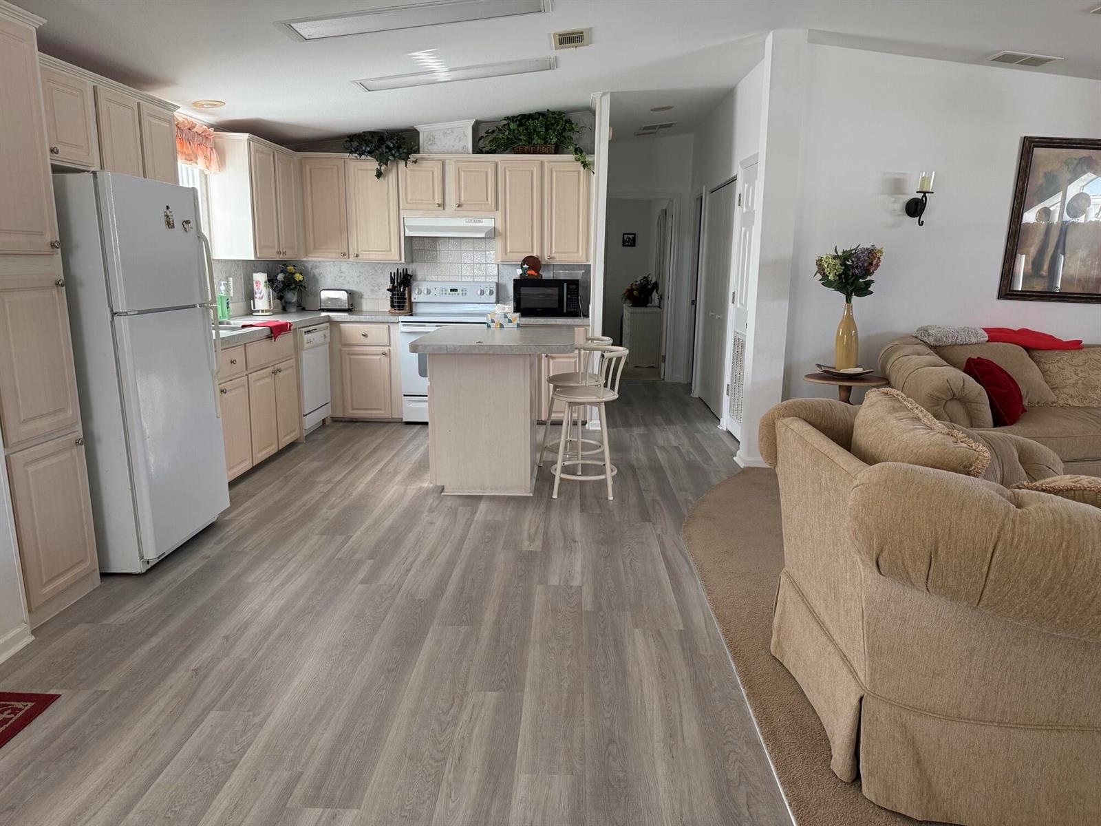 An open-concept kitchen with light wood cabinets and a small island overlooks a living area — 6615 Spanish Lakes Boulevard, Fort Pierce FL 34951, FORT PIERCE, FL
