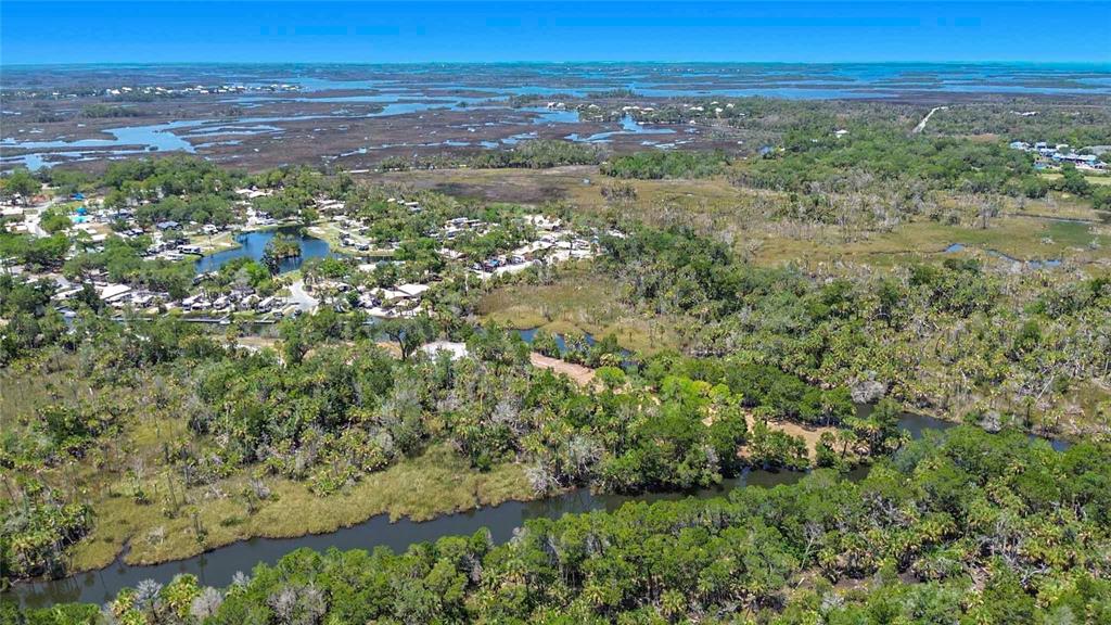 An aerial view shows a wooded landscape with a winding creek and a nearby residential community — 11441 W BROWN PELICAN PATH, CRYSTAL RIVER, FL