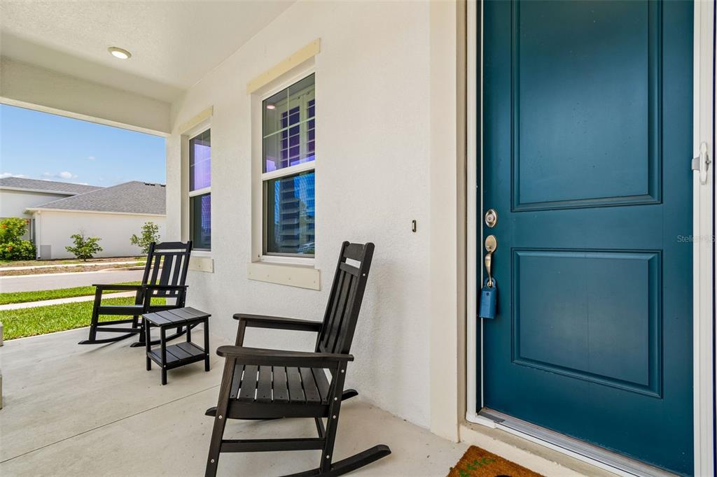 A covered front porch features two black rocking chairs and a teal front door — 283 SAND CRANE WAY, TARPON SPRINGS, FL