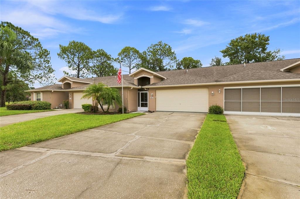 A view of the exterior of a tan-colored duplex with a shared concrete driveway — 7411 MOORGATE COURT, NEW PORT RICHEY, FL