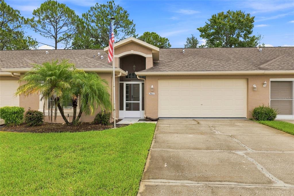 A single-story house with a beige stucco exterior, a two-car garage, and a front entryway — 7411 MOORGATE COURT, NEW PORT RICHEY, FL