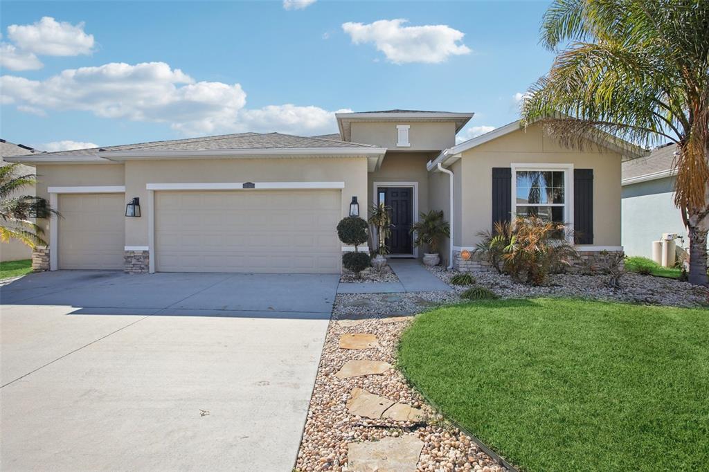 A single-story suburban house features a tan stucco exterior, a three-car garage, and landscaping — 10747 LAXER CAY LOOP, SAN ANTONIO, FL