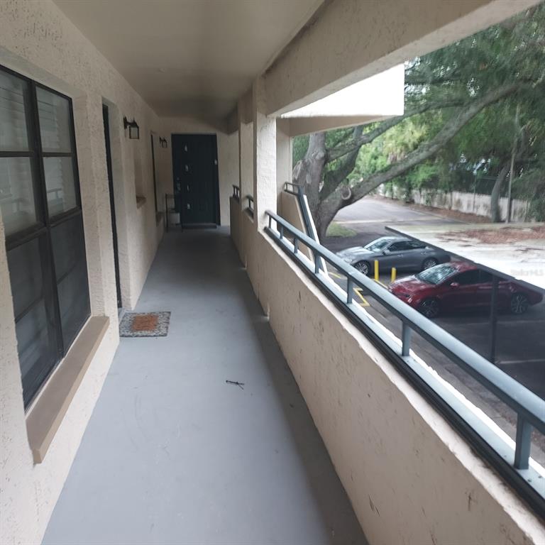 An outdoor apartment walkway features a gray floor, a dark door, and a metal railing — 4927 PURITAN CIRCLE UNIT 123, TAMPA, FL