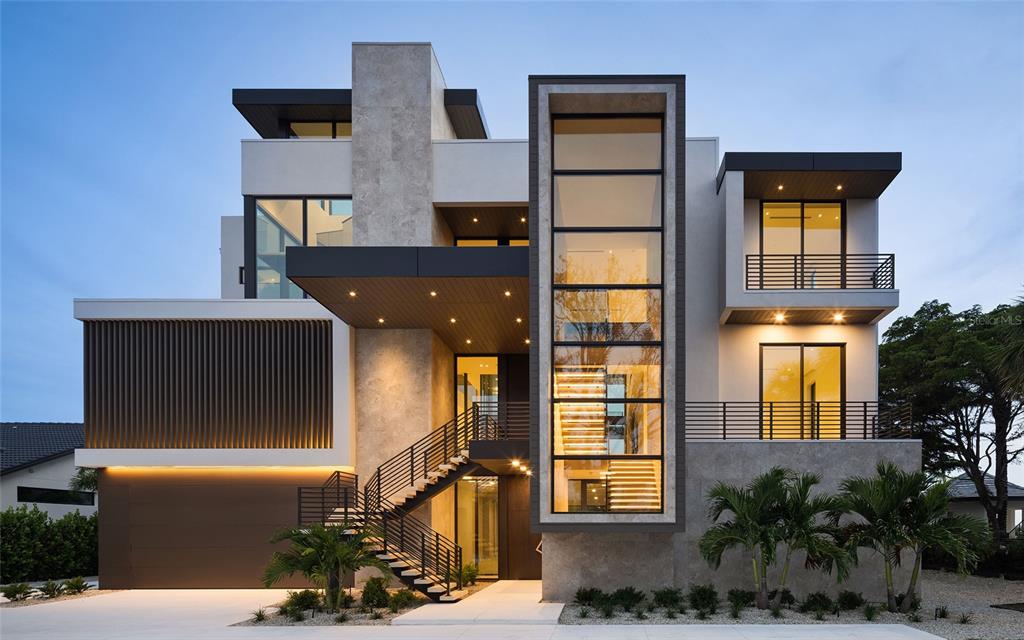 A modern three-story house features a prominent glass stairwell, stone accents, and an exterior staircase — 388 S SHORE DRIVE, SARASOTA, FL