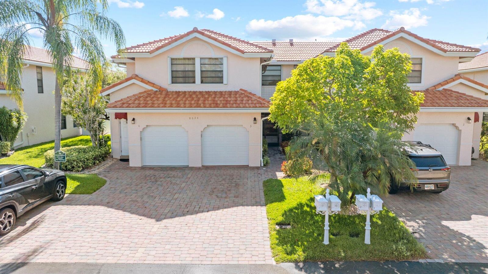 An exterior view of a two-story residential building with two garage doors and a paved driveway — 8634 Via Reale # 3, Boca Raton FL 33496, BOCA RATON, FL