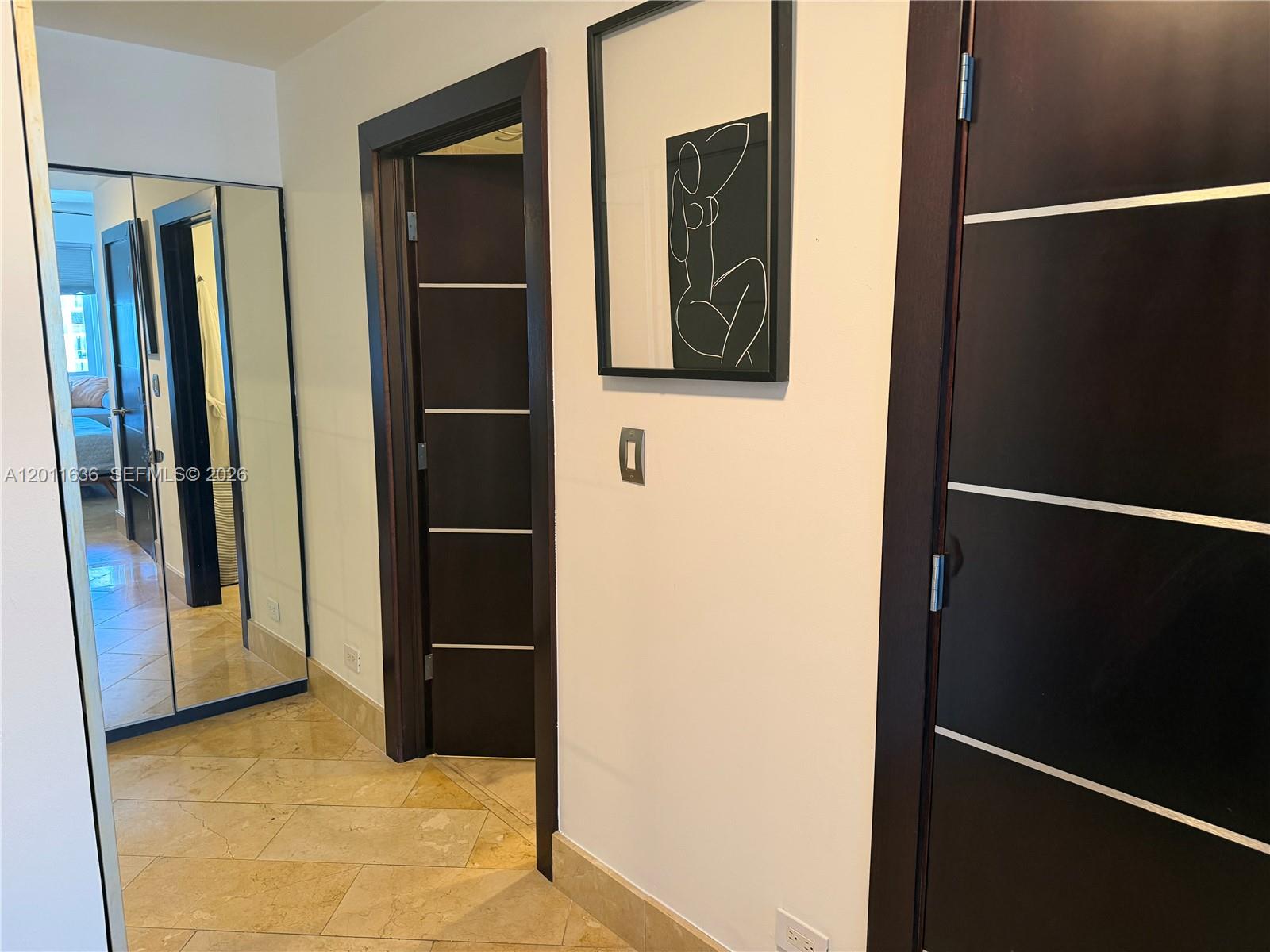 A hallway features tiled floors, dark wood doors with silver accents, and framed wall art — 2301 Collins Ave, Miami Beach FL 33139, MIAMI BEACH, FL