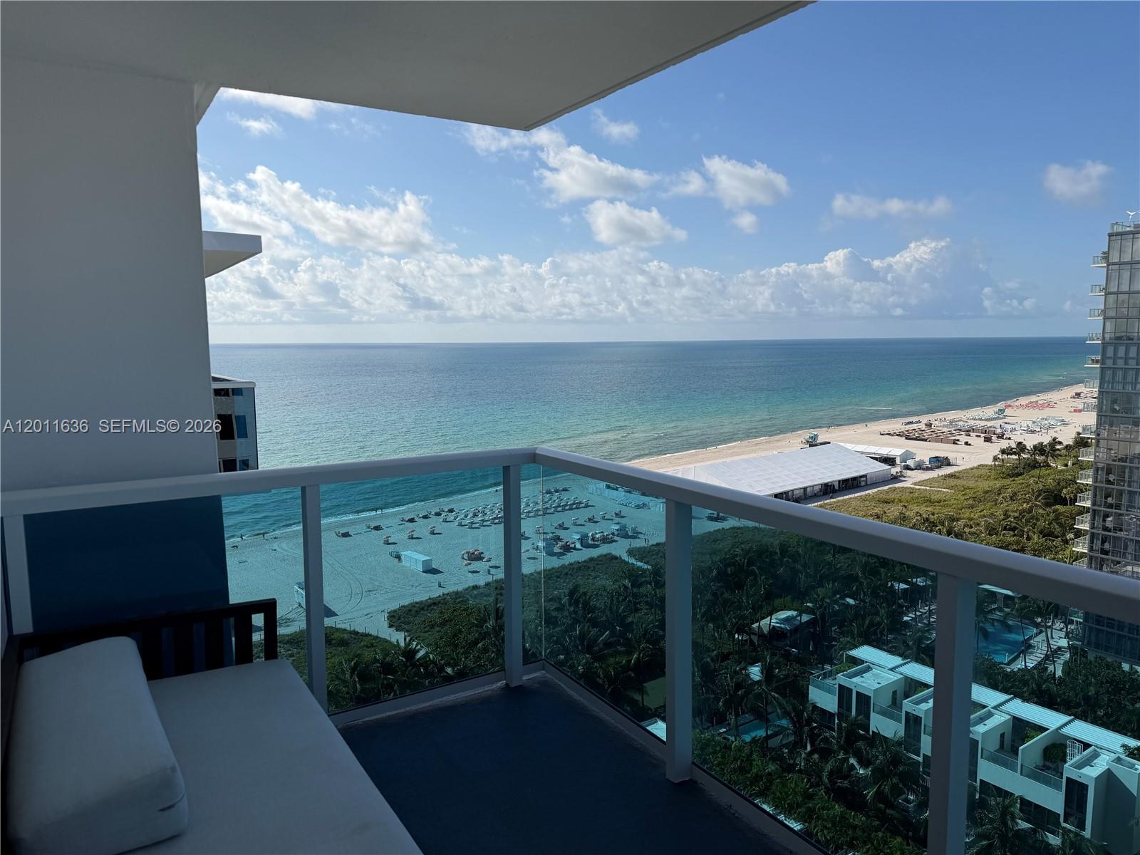 A balcony with a glass railing overlooks a beach, ocean, and coastal buildings — 2301 Collins Ave, Miami Beach FL 33139, MIAMI BEACH, FL