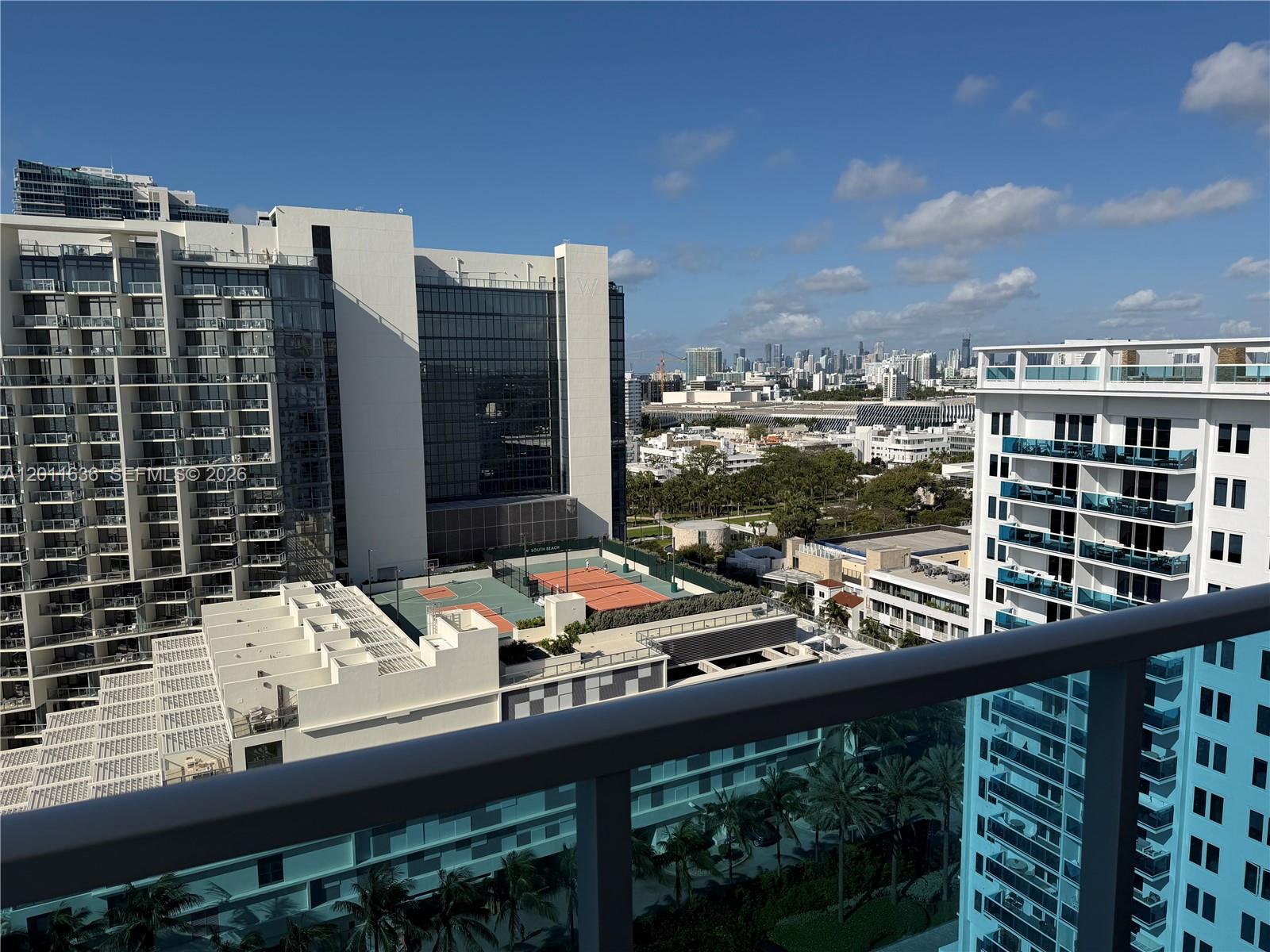 A high-angle view from a balcony shows nearby apartment buildings, a tennis court, and a distant city skyline — 2301 Collins Ave, Miami Beach FL 33139, MIAMI BEACH, FL