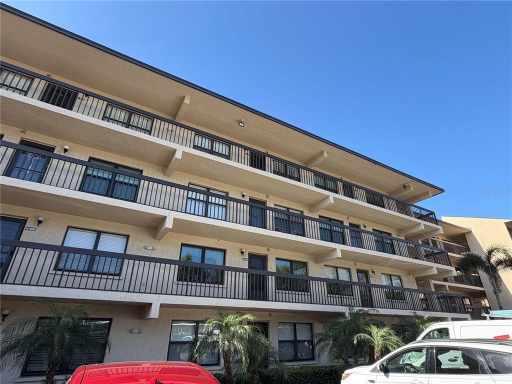 A low-angle exterior view of a multi-story apartment building with balconies and palm trees — 515 W 30TH AVENUE UNIT 405-H, BRADENTON, FL