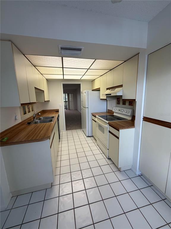 A galley kitchen features white cabinets, wood-look laminate countertops, and white tile flooring — 515 W 30TH AVENUE UNIT 405-H, BRADENTON, FL
