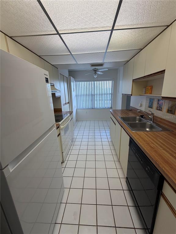 A galley kitchen features white appliances, wood-look laminate countertops, and white tile flooring — 515 W 30TH AVENUE UNIT 405-H, BRADENTON, FL