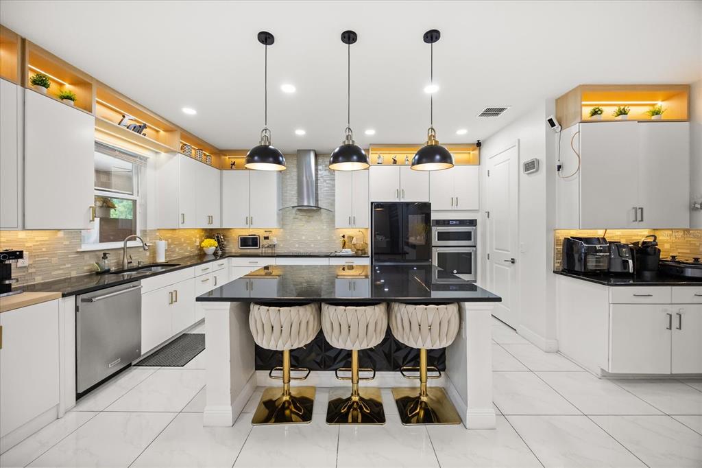 A modern kitchen features white cabinetry, black countertops, a central island with stools, and pendant lighting — 8109 LUDINGTON CIRCLE, ORLANDO, FL