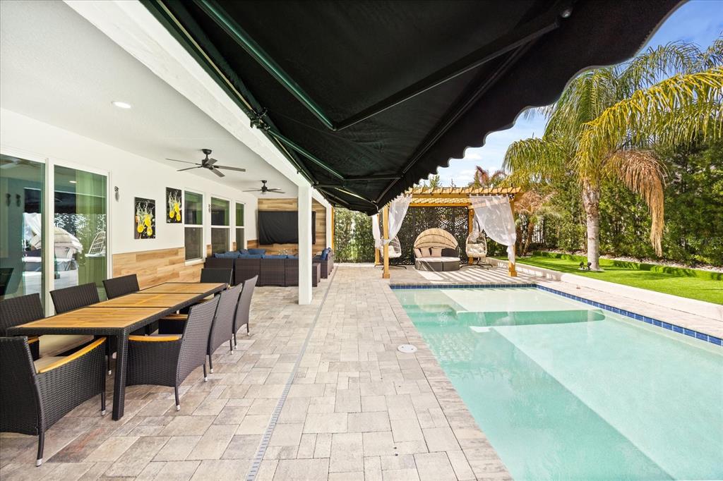 A covered patio with a dining set and pool overlooks a backyard with a pergola — 8109 LUDINGTON CIRCLE, ORLANDO, FL