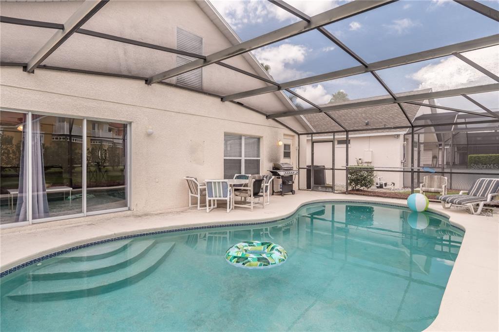A swimming pool with a screen enclosure and patio furniture sits behind a residential home — 4609 FORMBY COURT, KISSIMMEE, FL