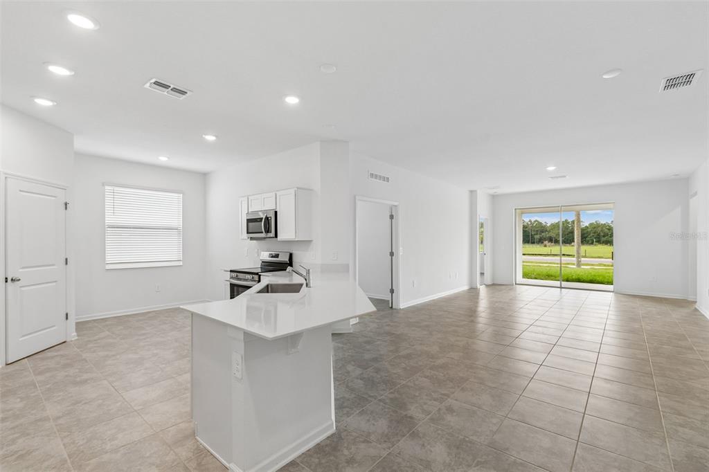 An open-concept kitchen and living area with white cabinets, quartz countertops, and tile flooring — 1676 TEAGAN LANE, WINTER HAVEN, FL