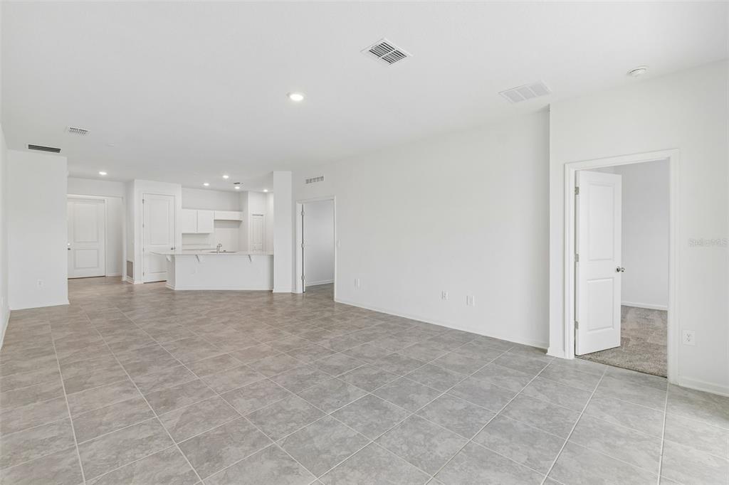 An open-concept living area features gray tile flooring, white walls, and an adjacent kitchen — 1676 TEAGAN LANE, WINTER HAVEN, FL