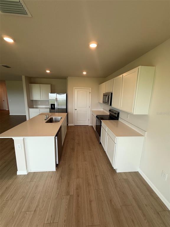 A modern kitchen features white cabinets, a large island, stainless steel appliances, and wood-look flooring — 11003 44TH AVENUE E, PALMETTO, FL