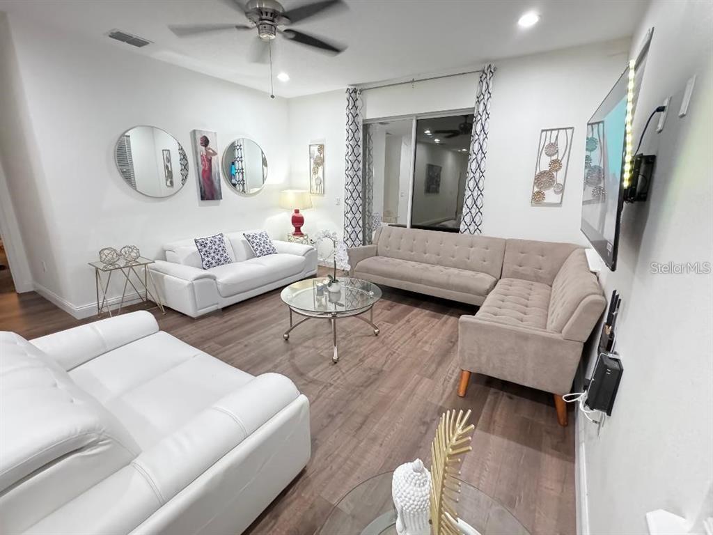 A living room features white and beige sofas, a glass coffee table, and wood flooring — 821 LAND AVENUE, LONGWOOD, FL