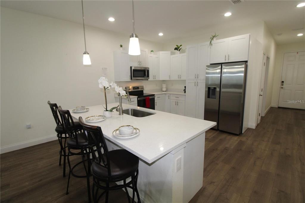 A modern kitchen features white cabinets, stainless steel appliances, and a large quartz-topped island — 821 LAND AVENUE, LONGWOOD, FL
