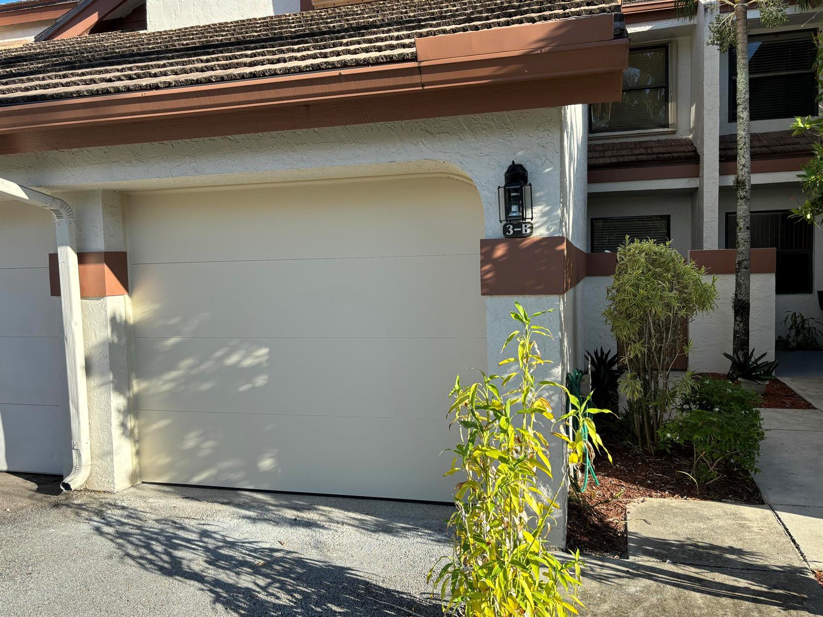 A beige garage door with a black lantern light fixture on a stucco building exterior — 12692 Shoreline Drive # 3b, Wellington FL 33414, WELLINGTON, FL