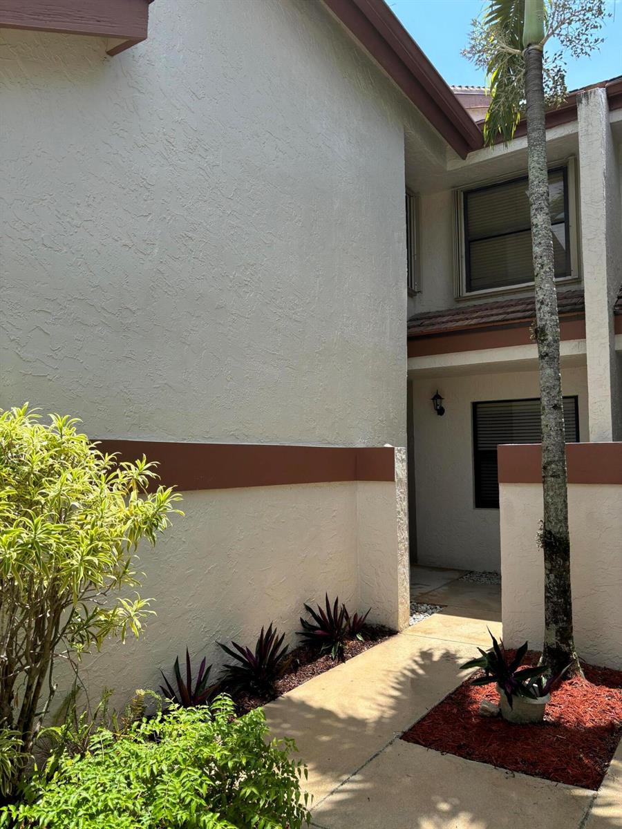 A concrete walkway leads to the entrance of a two-story stucco home with brown trim — 12692 Shoreline Drive # 3b, Wellington FL 33414, WELLINGTON, FL