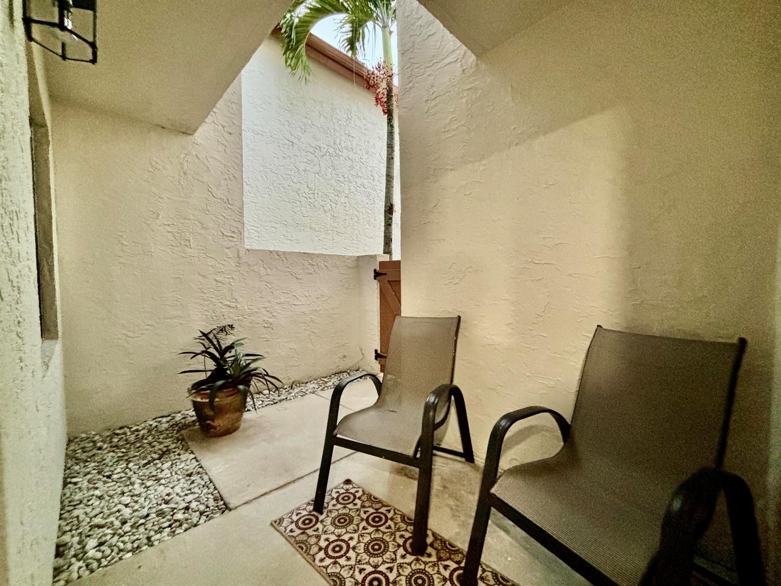 A small, enclosed outdoor patio features two chairs, a potted plant, and gravel landscaping — 12692 Shoreline Drive # 3b, Wellington FL 33414, WELLINGTON, FL