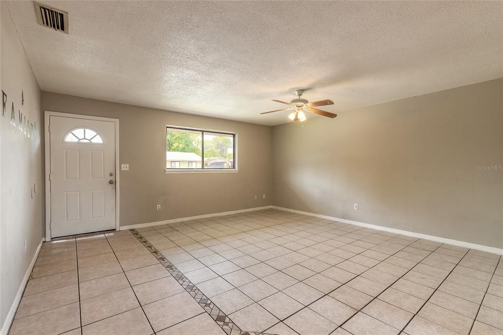 An empty living room features beige walls, a ceiling fan, and light-colored tiled flooring — 632 LPGA BOULEVARD UNIT B, DAYTONA BEACH, FL