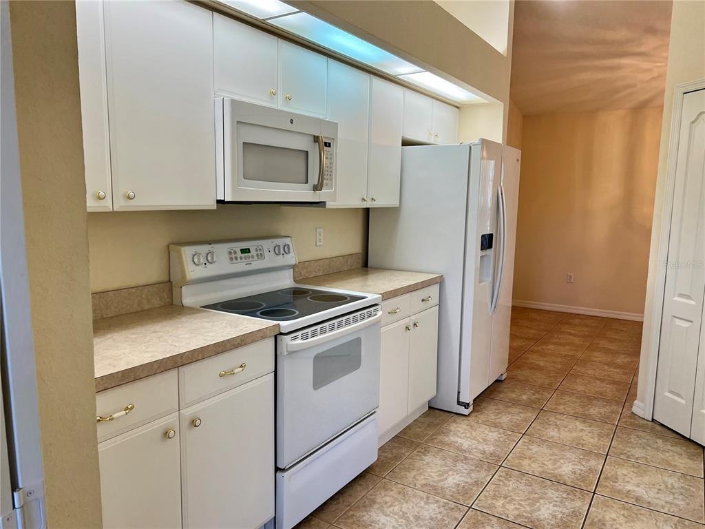A kitchen features white cabinets, white appliances, and tan countertops over tiled flooring — 6795 DAVID BOULEVARD UNIT A, PORT CHARLOTTE, FL