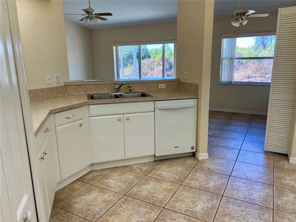 A kitchen with white cabinets, a double sink, and tile flooring overlooks an adjacent room — 6795 DAVID BOULEVARD UNIT A, PORT CHARLOTTE, FL