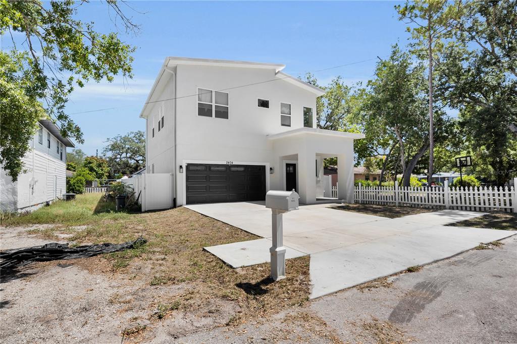 A two-story white house with a black garage door and a white picket fence — 2404 CASSELL, TAMPA, FL