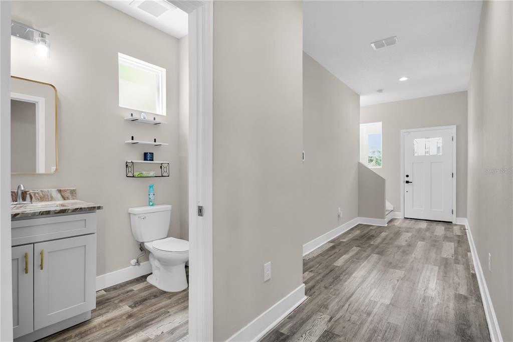 A hallway with wood-look flooring leads to a front door and an adjacent half bathroom — 2404 CASSELL, TAMPA, FL