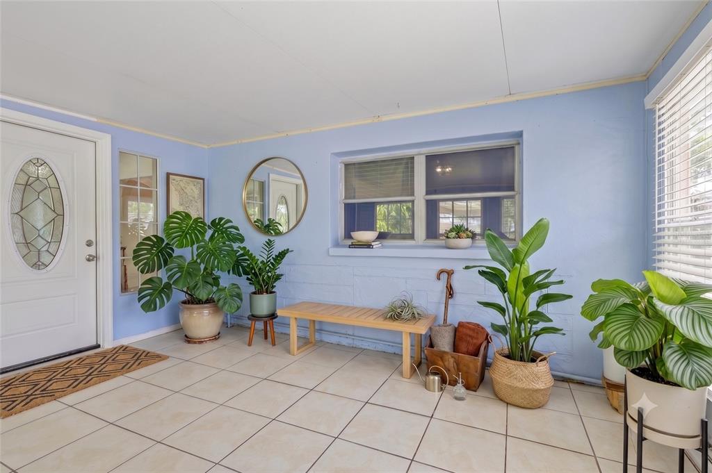 A light blue sunroom features tiled floors, a wooden bench, and several potted indoor plants — 9680 PARK LAKE DRIVE N, PINELLAS PARK, FL