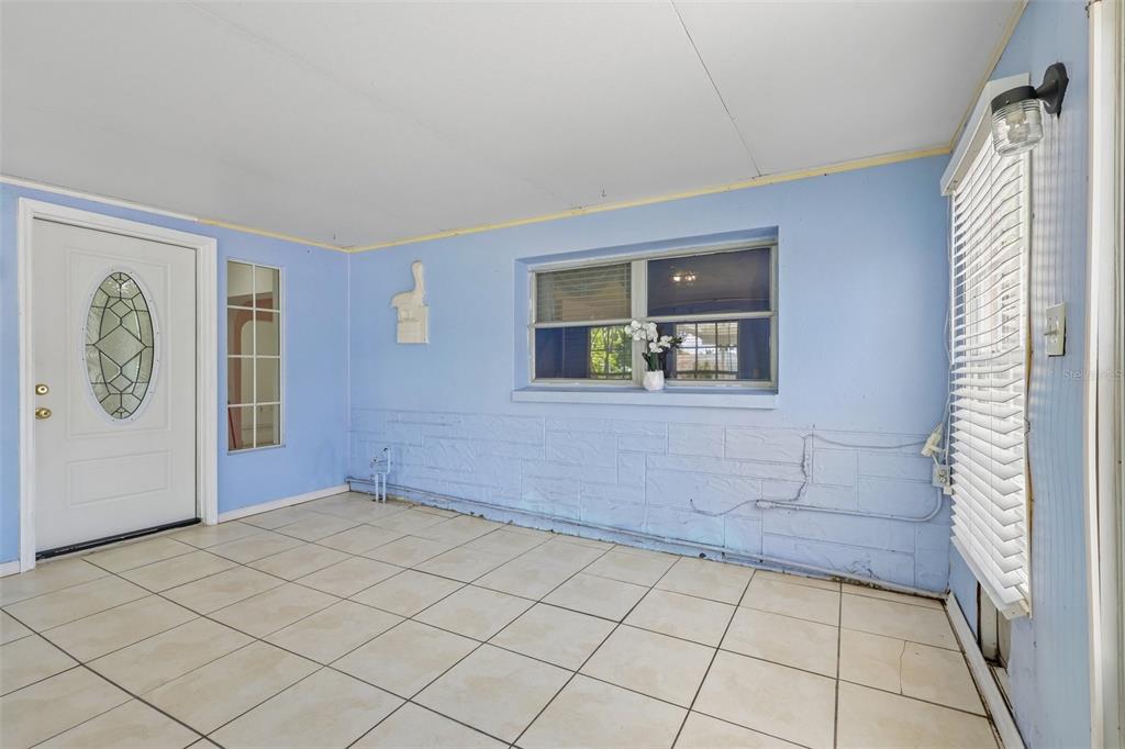A sunroom with light blue walls, white tiled floors, a white door, and a window — 9680 PARK LAKE DRIVE N, PINELLAS PARK, FL