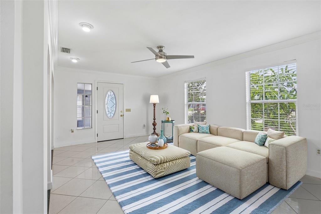 A living room with tile floors, a sectional sofa, a striped rug, and a front door — 9680 PARK LAKE DRIVE N, PINELLAS PARK, FL