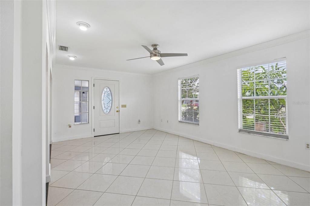 A bright, empty room with white walls, tiled floors, a ceiling fan, and two windows — 9680 PARK LAKE DRIVE N, PINELLAS PARK, FL
