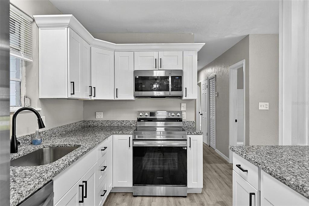 A kitchen features white cabinets, granite countertops, stainless steel appliances, and light wood-look flooring — 610 ROMA STREET, DAYTONA BEACH, FL