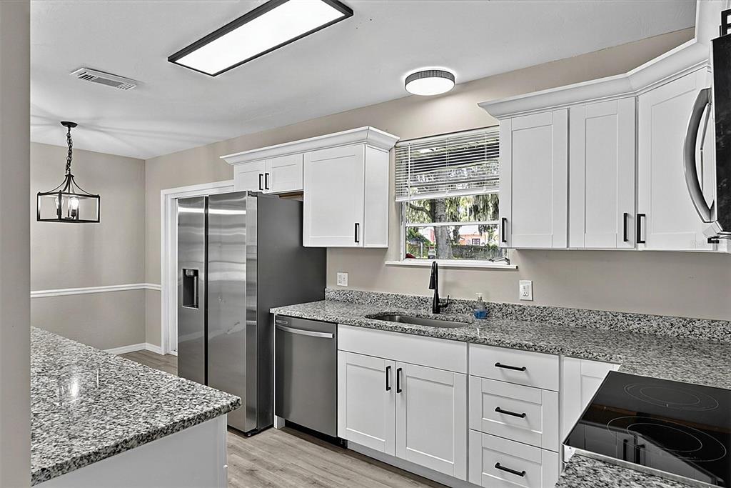 A kitchen features white cabinets, granite countertops, stainless steel appliances, and a window over the sink — 610 ROMA STREET, DAYTONA BEACH, FL