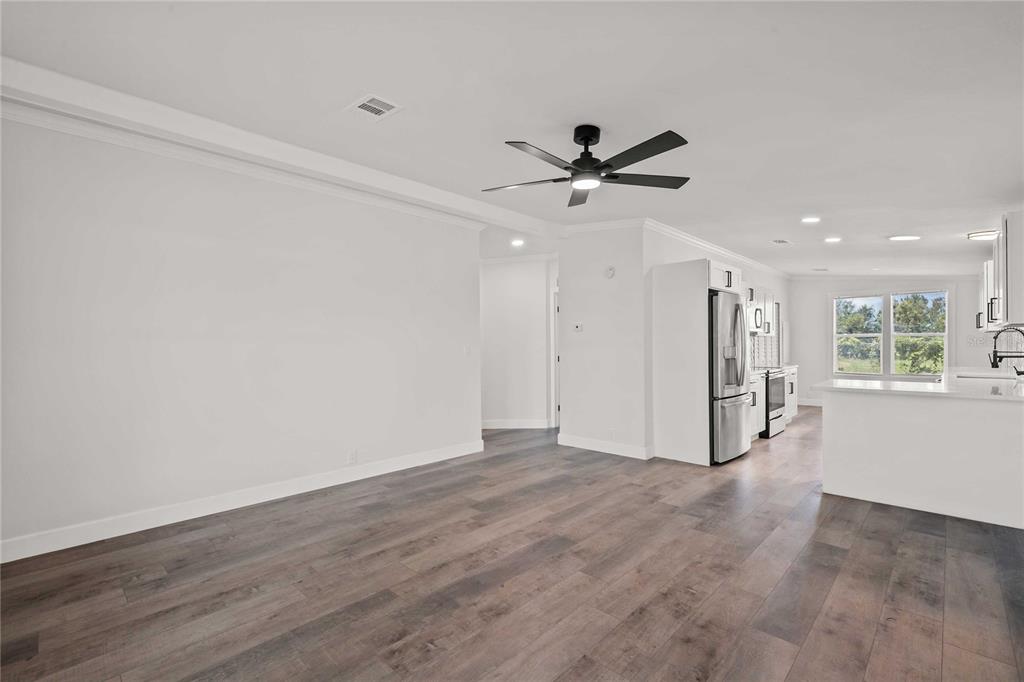 An open-concept living area with wood-look flooring, a ceiling fan, and an adjacent white kitchen — 34010 ESTATES LANE, WESLEY CHAPEL, FL