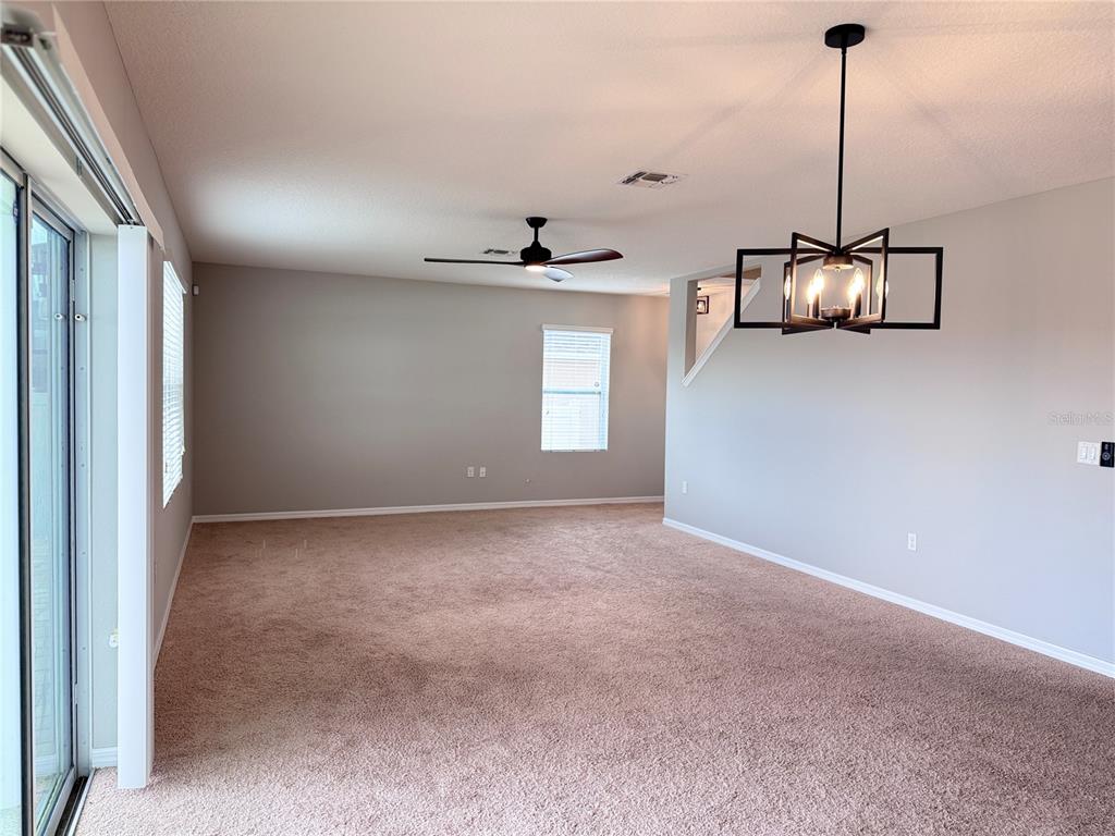 An empty living room features beige carpet, a ceiling fan, and a modern geometric chandelier — 362 NOVA DRIVE, DAVENPORT, FL
