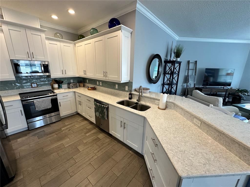 A kitchen features white cabinets, light countertops, a tiled backsplash, and wood-look tile flooring — 7730 34TH AVE W UNIT 303, BRADENTON, FL
