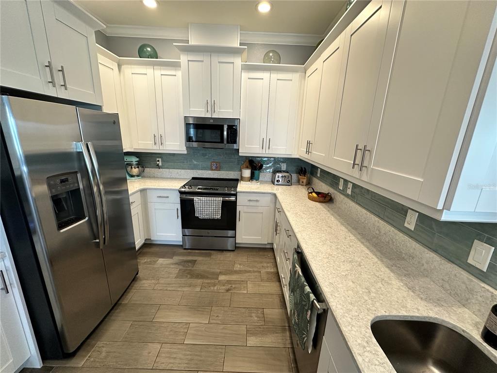 A kitchen features white cabinetry, stainless steel appliances, light countertops, and a blue tile backsplash — 7730 34TH AVE W UNIT 303, BRADENTON, FL