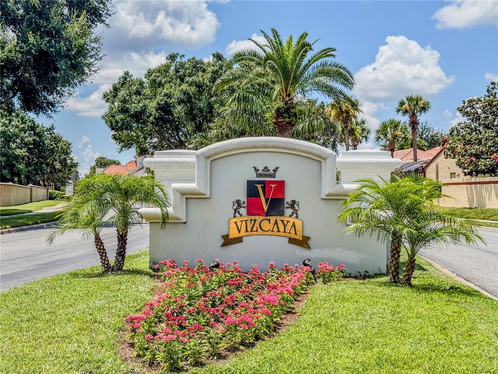 A community entrance sign for Vizcaya features a crest, palm trees, and a flower bed — 8755 THE ESPLANADE UNIT 130, ORLANDO, FL
