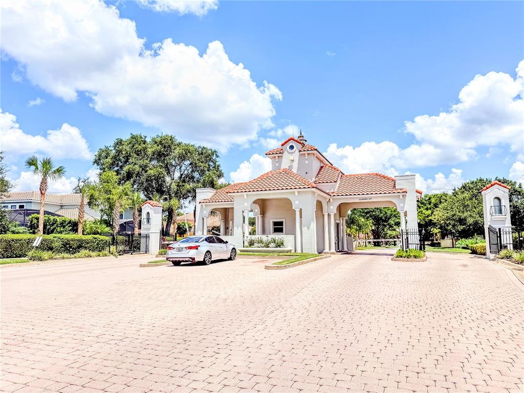A silver sedan is parked in front of a gated community entrance with a tiled roof — 8755 THE ESPLANADE UNIT 130, ORLANDO, FL