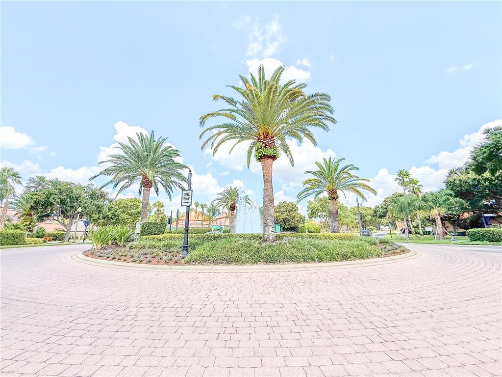 A paved roundabout features a central garden with palm trees and a water fountain — 8755 THE ESPLANADE UNIT 130, ORLANDO, FL
