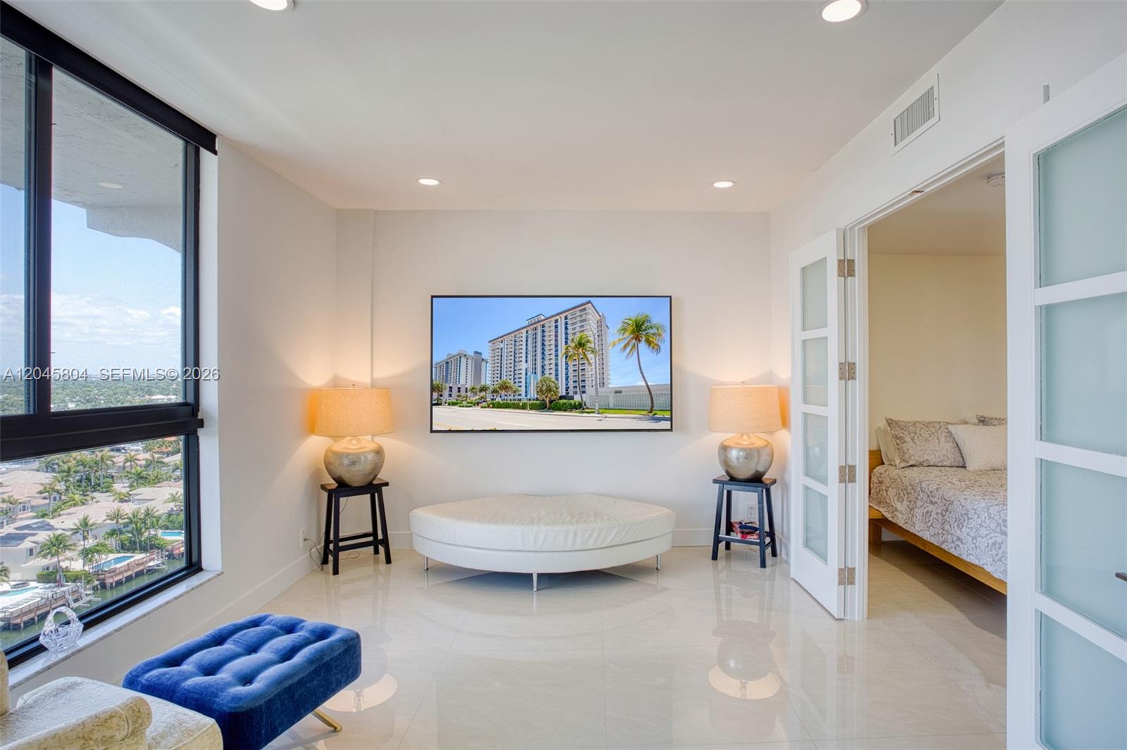 A bright room features a white circular ottoman, a wall-mounted television, and tiled flooring — 1500 S Ocean Dr, Hollywood FL 33019, HOLLYWOOD, FL